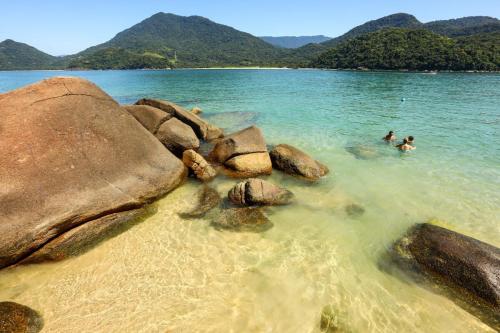 two people swimming in the water near some rocks at Casa Azul Jaraguá in São Sebastião