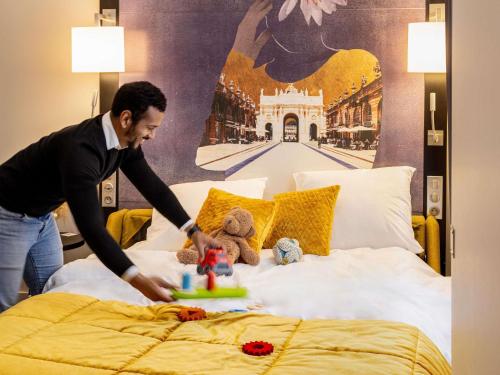 a man making a bed in a hotel room at Mercure Nancy Centre Place Stanislas in Nancy