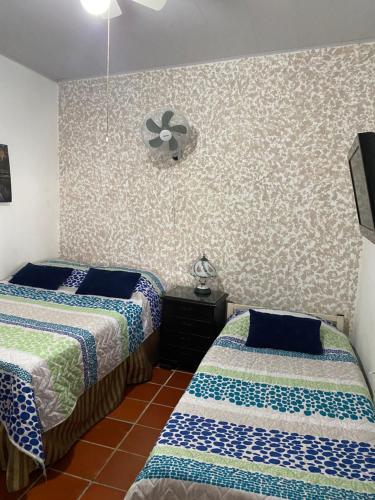 a bedroom with two beds and a fan on the wall at La Casa de Luzma in Pueblo Bello