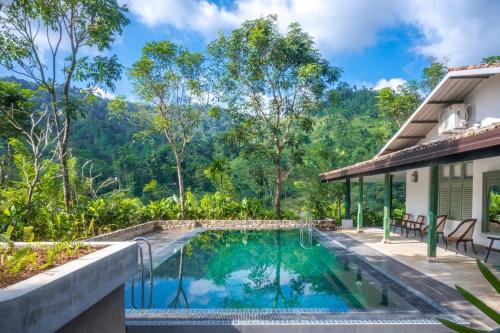 a swimming pool in front of a house with mountains in the background at Sinharaja River Lodge in Nikawatawana