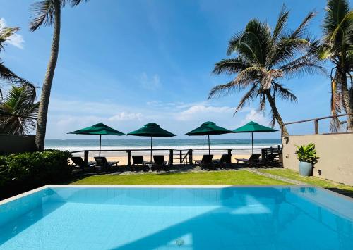 a swimming pool in front of a beach with umbrellas at Hikka House - Thema Collection in Hikkaduwa