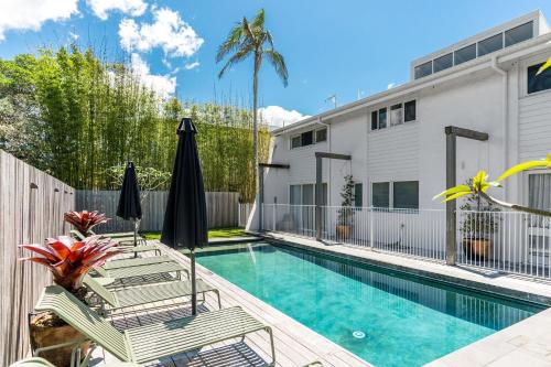 a pool with chairs and umbrellas next to a house at Barbara by Kinsfolk in Byron Bay
