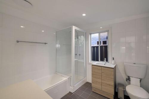 a white bathroom with a tub and a toilet and a sink at Casa Esperanza by Experience Jervis Bay in Vincentia