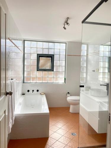 a white bathroom with a tub and a toilet at Cronulla courtyard unit, 10 mins walk to Beach & Bay in Cronulla