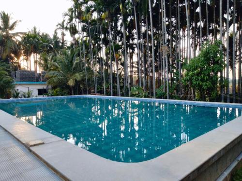 a swimming pool in front of a fence with trees at Saatvik Stay 2 - A Dormitory Stay in Kushālnagar