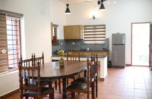 a kitchen with a wooden table with chairs and a refrigerator at Acrewood Farmhouse - Pool Villa in Vāzhākulam