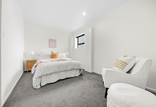 ein weißes Schlafzimmer mit einem Bett und einem Stuhl in der Unterkunft Spacious 3-Bedroom Retreat Near Airport & City in Auckland