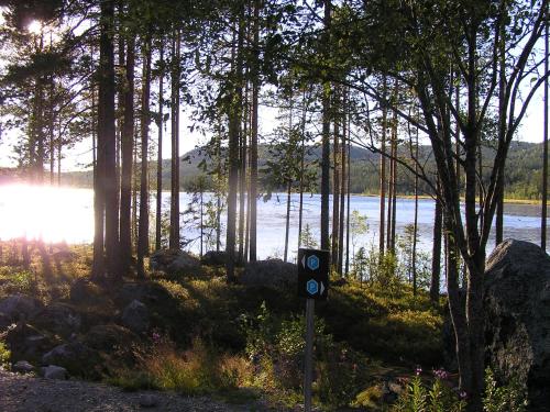 a sign next to a body of water with trees at Fredrika Hotell Jakt&Fiskecamp in Fredrika