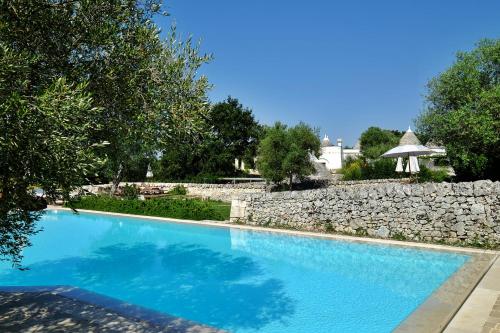a large blue swimming pool next to a stone wall at Masseria Trulli e Vigne in Martina Franca