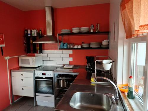Una cocina con paredes rojas, un fregadero y una estufa. en Grundarfjördur Hostel, en Grundarfjordur