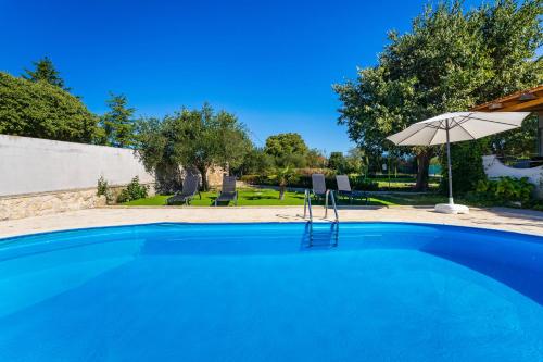 a blue swimming pool with an umbrella and chairs at My Dalmatia - Holiday home Emily with private pool in Raštević