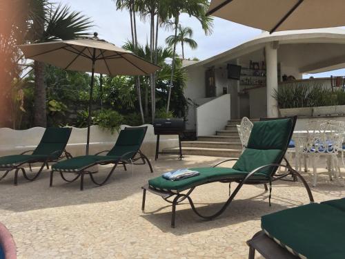 a group of chairs and umbrellas in front of a house at Villa Palmitas acogedor departamento nivel piscina gigante jardines in Acapulco