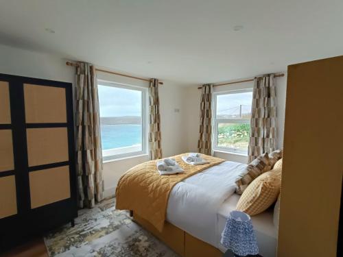 a bedroom with a bed and two large windows at Ocean Edge in Sennen Cove