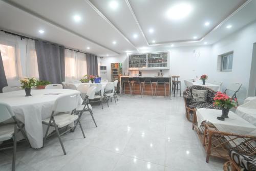 a dining room with white tables and chairs and a kitchen at Résidence Keur Antou in Ziguinchor