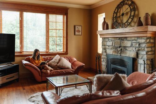 a woman sitting on a couch in a living room with a fireplace at Chalet Alpin Walk to Lake and Beach with Spa and BBQ in Huberdeau