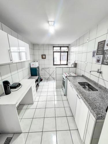 a white tiled kitchen with a sink and counters at Hospedatom - Apartamento Economy Prainha Arraial do Cabo in Arraial do Cabo