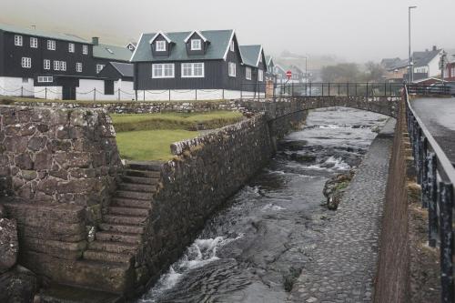 Un puente de piedra sobre un río con casas al fondo. en Toftarstova - Seaview - Historic - 3BR House, en Kvívík