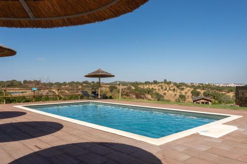 a swimming pool with an umbrella on a patio at Monte Clérigo Casas de Campo in Almodôvar