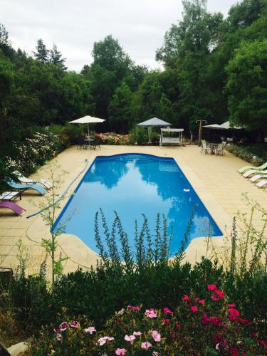 a blue swimming pool in a garden with tables and umbrellas at Cabañas Rahue in Vilches