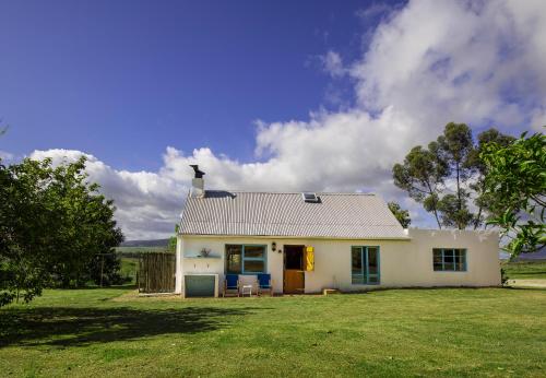 a small white house on a grass field at Beloftebos Farm Cottages in Papiesvlei