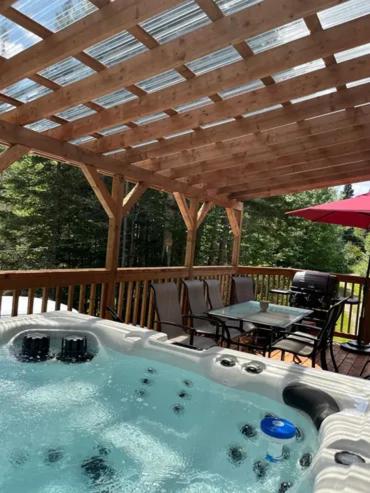 een hottub onder een houten terras met een tafel bij Chalet Le Mona in Notre-Dame-Des-Bois