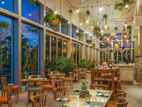 un restaurante con mesas, sillas y ventanas en Grand Mercure Danang, en Da Nang