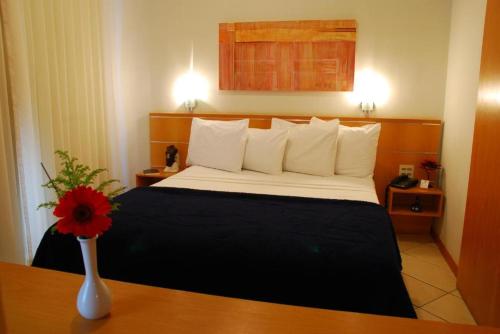 a hotel room with a bed and a vase with a flower at Vila da Serra Differential in Nova Lima