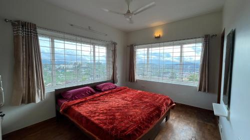 a bedroom with a red bed and two windows at Vivens Villas in Ooty