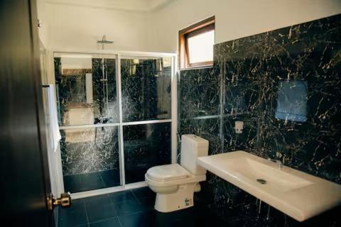 a black tiled bathroom with a toilet and a sink at Thomasz Lodge 2 in Kandy