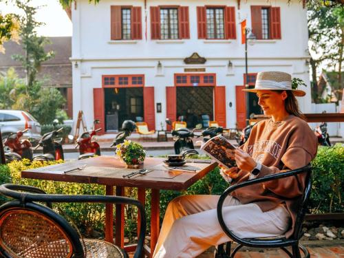 una mujer sentada en una mesa leyendo un libro en 3 Nagas Hotel Luang Prabang - MGallery Collection, en Luang Prabang