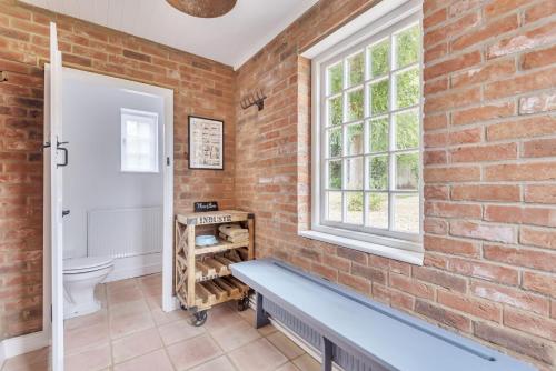 a brick walled bathroom with a bench and a window at The Long Cottage with attic in Flitcham