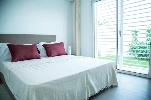 a white bed with red pillows in a room with a window at Modern with garden 5mn from Carthage and Lac in Sidi Daoud