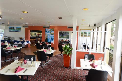 a restaurant with white tables and black chairs at Bundaberg International Motor Inn in Bundaberg