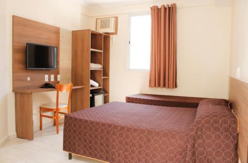 une chambre avec un lit, un bureau et une télévision dans l'établissement Hotel Guarumar, à Guarujá