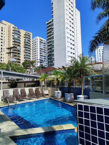 une piscine avec des chaises longues, des palmiers et des bâtiments dans l'établissement Hotel Guarumar, à Guarujá