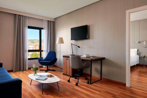 Una habitación de hotel con un escritorio, sillas y una cama. en NH Ciudad de Cuenca, en Cuenca