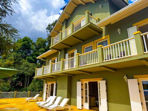 Villa Coração Guesthouse by Concavus في مونتي فيردي: مبنى أخضر مع كراسي بيضاء وشرفة