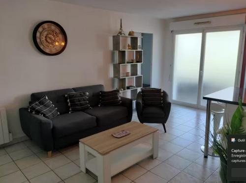 een woonkamer met een zwarte bank en een tafel bij Appartement avec parking privé in Aytré