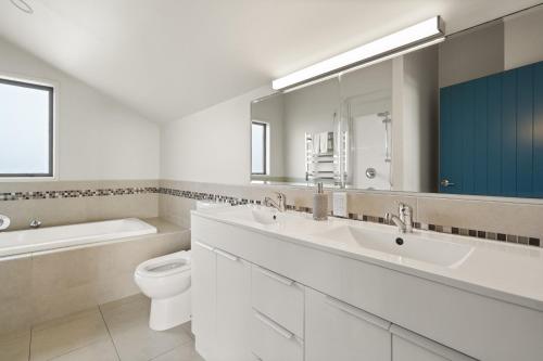 een badkamer met 2 wastafels, een toilet en een spiegel bij Mangonui Ridge Retreat in Mangonui
