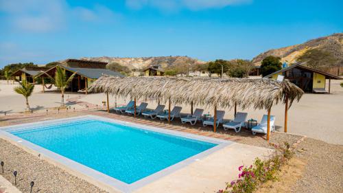 a swimming pool with chairs and a straw hut at Wallac Bungalows Canoas de Punta Sal in Canoas de Punta Sal