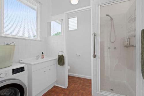 a white bathroom with a shower and a washing machine at Seascape On Cairnes in Indented Head