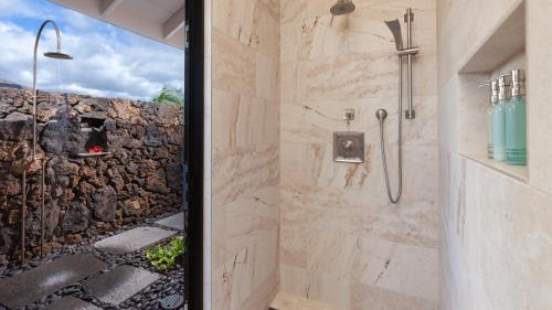 a bathroom with a walk in shower next to a stone wall at ALOHA SHORES Spacious Ainamalu 4BR Home with Mountain and Ocean View in Waikoloa