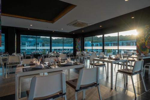 a restaurant with white tables and chairs and windows at Utopia Lofts by Sabai Sands in Nai Harn Beach