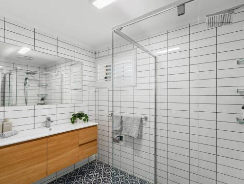 a white tiled bathroom with a sink and a shower at Coledale Beach Escape - Modern Comfort by the Sea in Coledale