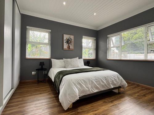 a bedroom with a large bed and two windows at Prospect Cottage B in Gqeberha
