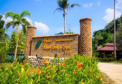 a sign for a hotel with palm trees and flowers at Hotel Khaosok and Spa in Khao Sok