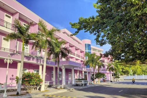 un bâtiment rose avec des palmiers en face d'une rue dans l'établissement Khu Nghỉ Dưỡng Đoàn 298 - Khách Sạn 3 Tầng, à Long Hải