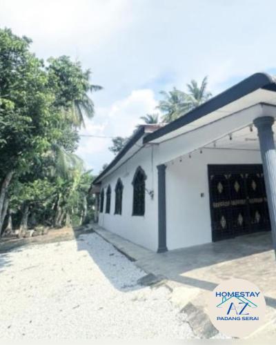 a white building with a garage with trees in the background at Homestay AZ Padang Serai in Padang Serai