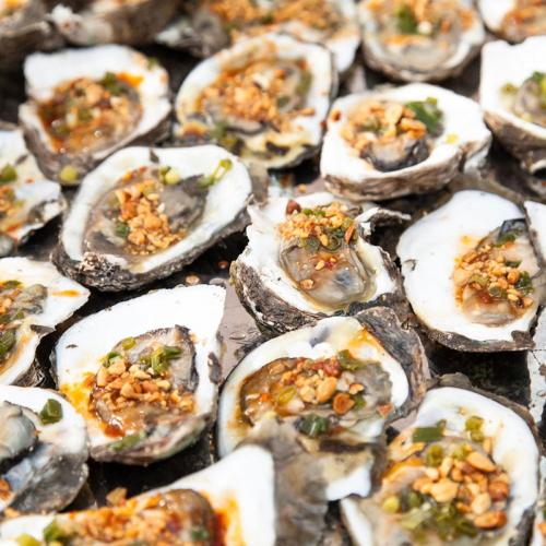 a bunch of oysters with ingrediants on a grill at New Pacific Hotel in Ho Chi Minh City