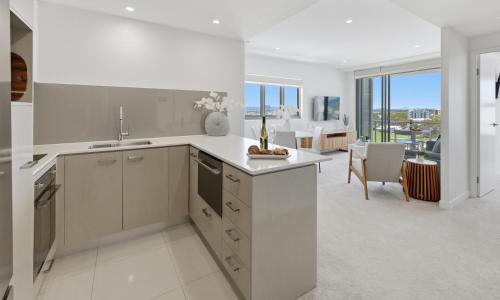 a kitchen with white cabinets and a living room at Verve on Cotton Tree managed by Sunny Coast Escapes in Maroochydore